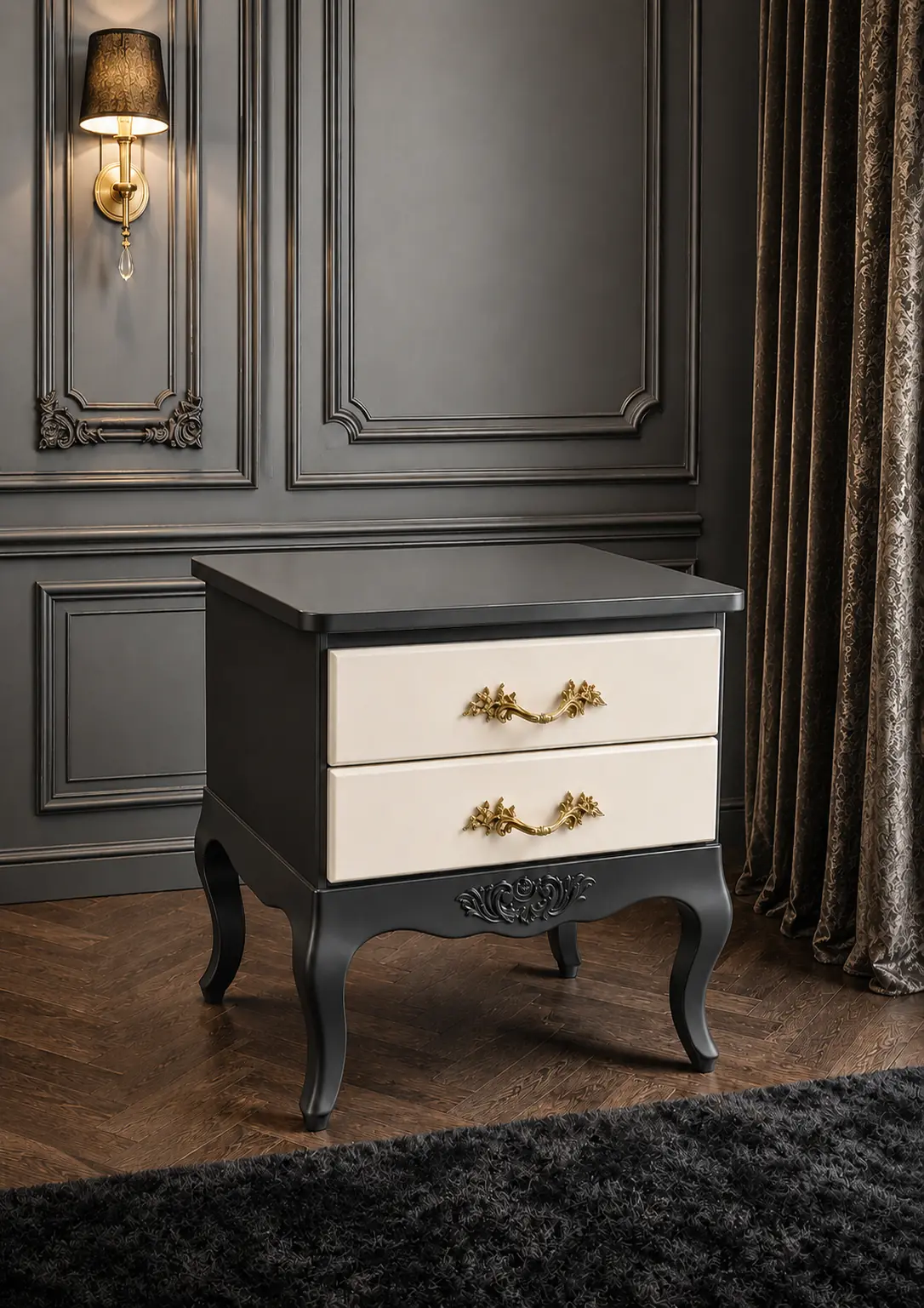 A vintage-style bedside table with black curved legs and sides, cream-coloured drawers with ornate gold handles, placed in an elegant, dark-panelled room with a wall sconce and heavy curtains.