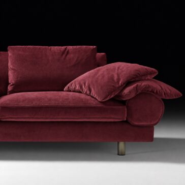 Burgundy Sofa with Retro Inspired Design Two matching scatter cushions resting on the rounded right arm, beside a piped seat and back cushion.