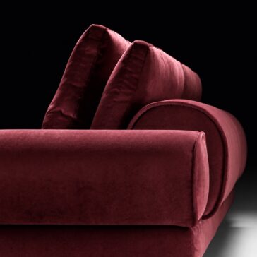 Burgundy Sofa with Retro Inspired Design Close-up of deep wine fabric, piped cushion edges and the curved bolster arm against a dark background.