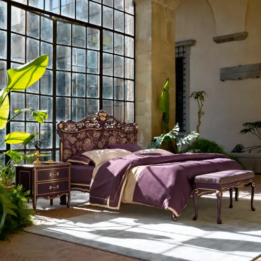 Deep amethyst upholstered Italian bed with a floral headboard and carved gold-trimmed frame in a sunlit bedroom